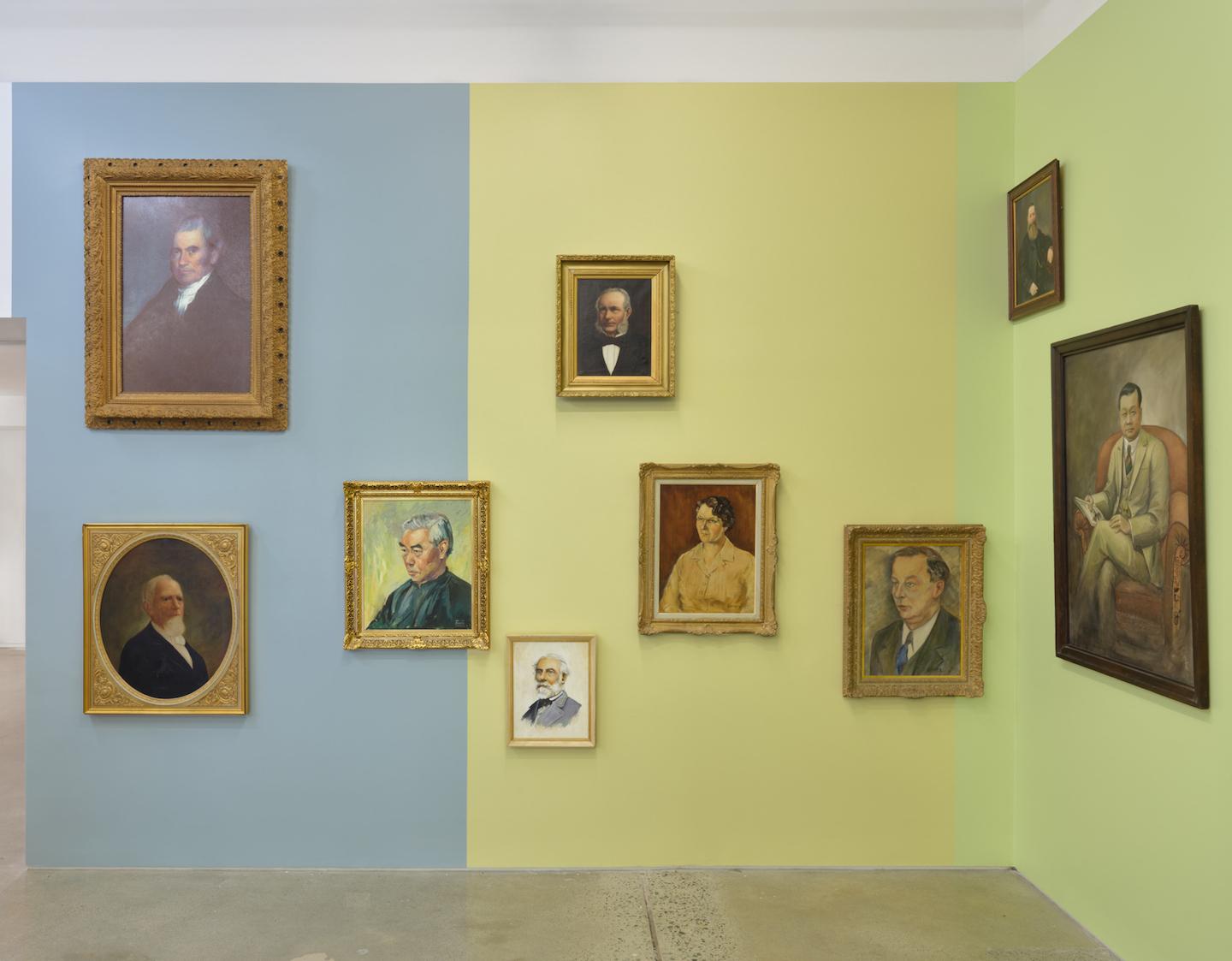 Nine portraits hang against dusty blue, wheaty yellow,  and pale green wall panels. The grey blues of ageing men’s hair tone with silk garments and yellow and green undertones surface between various skin shades. 