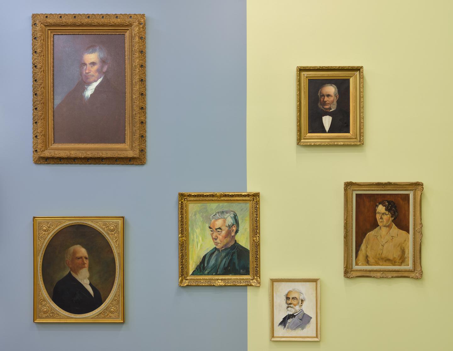 Six portraits hang against dusty blue and wheaty yellow wall panels. The grey blues of ageing men’s hair tone with silk garments and yellow and green undertones surface between various skin shades. 