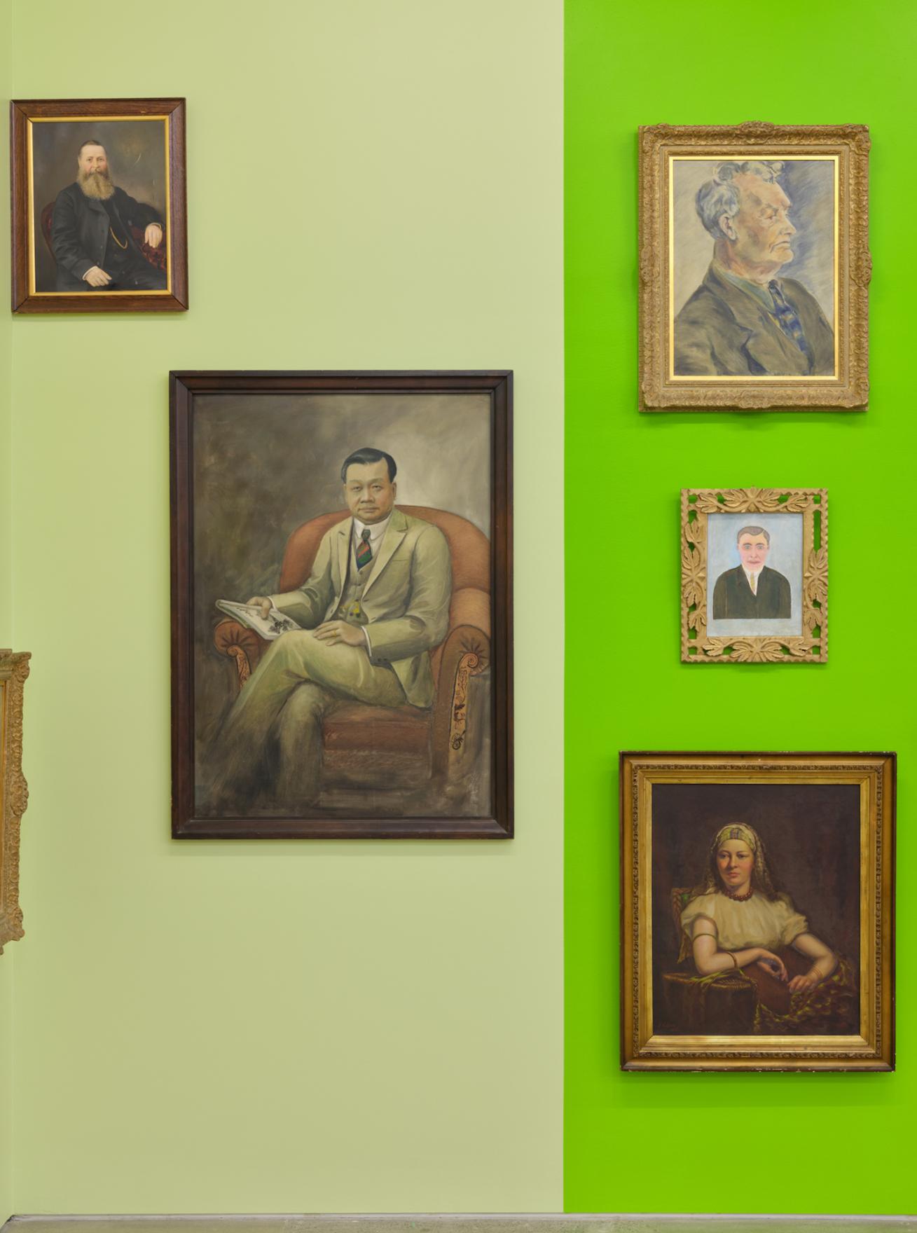 Five painted portraits with muted tones begin to pop against the pale green and acid green wall panels. As the blocks of colour are reflected faintly in each portrait’s colouration, a tonal theme begins to thread the disparate images together. 