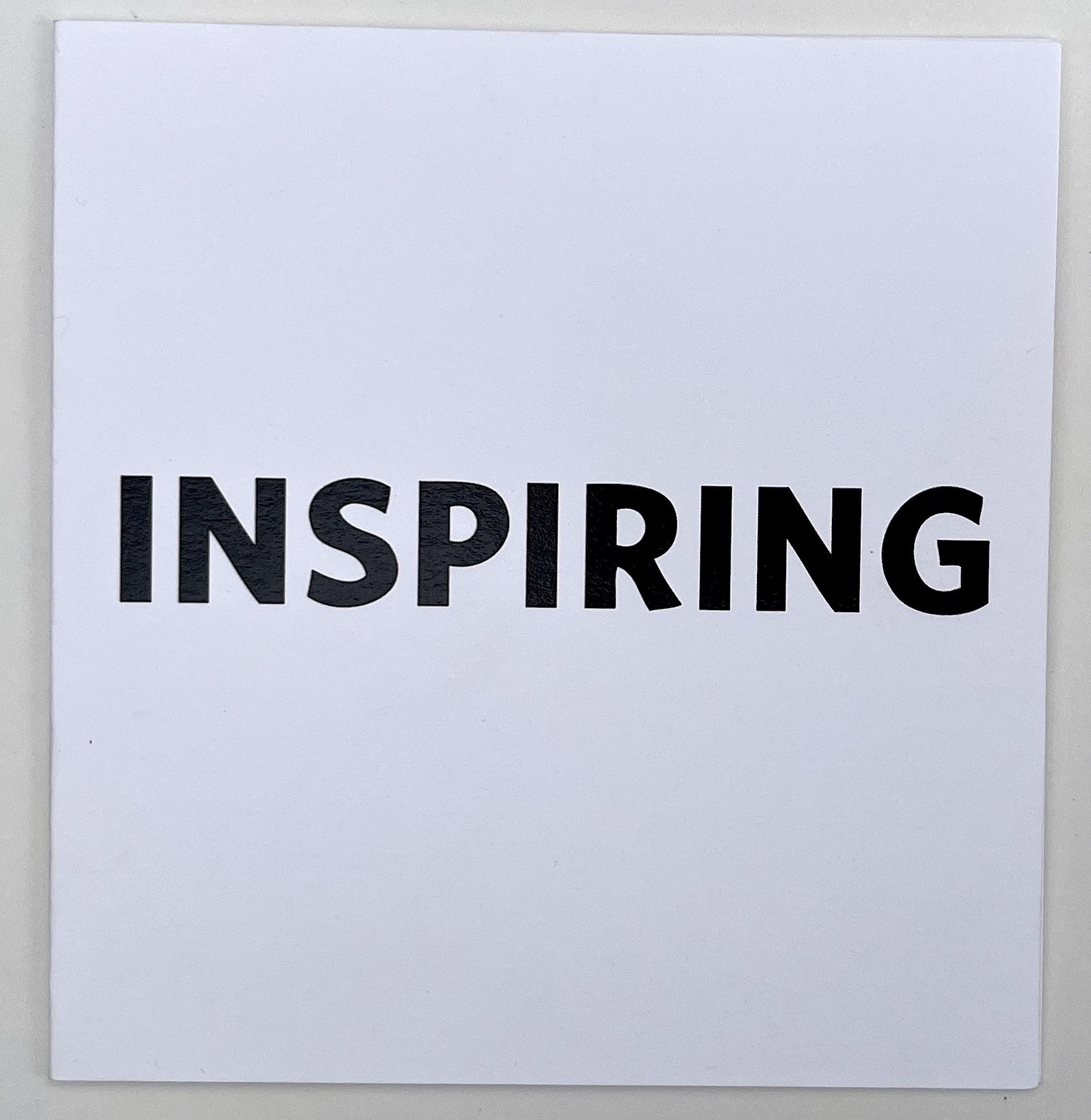 INSPIRING is written in bold black sans serif font across the center of a small square card stock folder. The block title asserts itself as a statement while withholding the context in it’s plainness. 