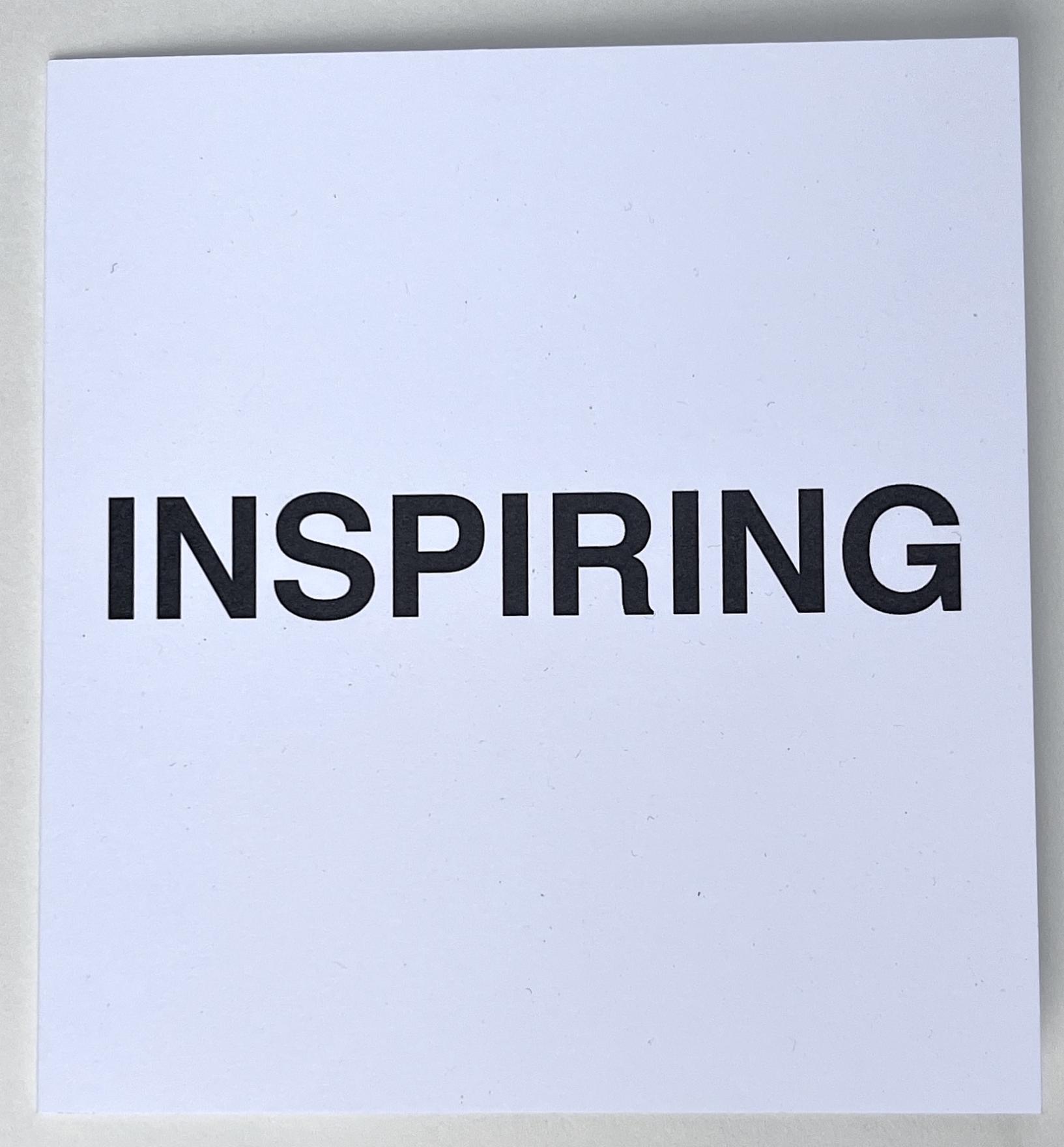  INSPIRING is written in bold black sans serif font across the center of a small square card stock folder. The block title asserts itself as a statement while withholding the context in it’s plainness. 