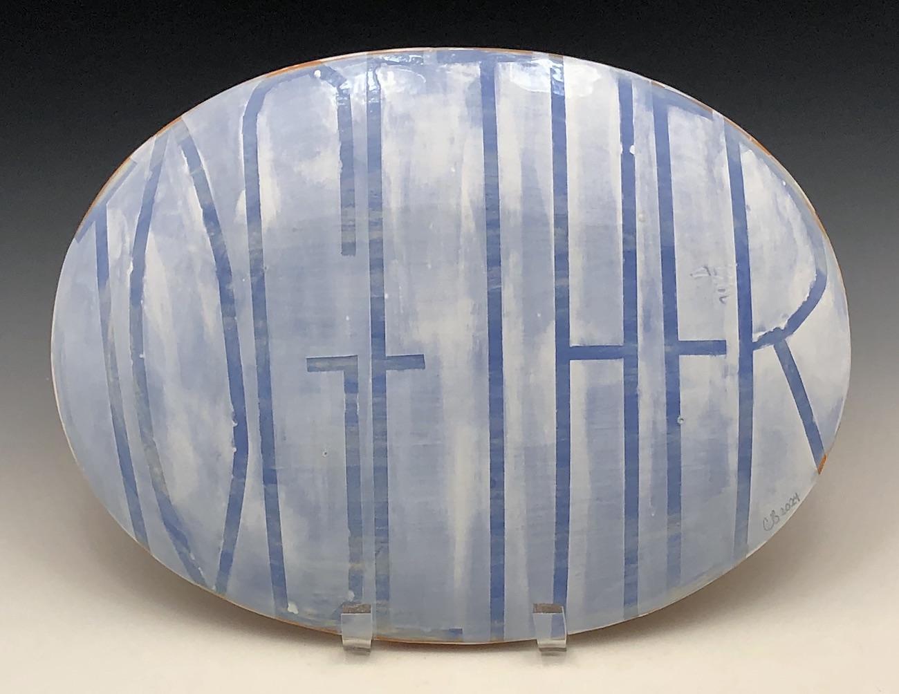 The backside of an ovular ceramic platter is painted in light blue and white. TOGETHER is written in thin tall lettering which swells to fit the convex shape.