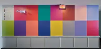  The apartment lobby wall is painted with 16 rectangular blocks of colour in a grid. The block on the top left is a light grey legend which lists the names of the colour blocks in slate grey text it reads: ON QUE IN PANTONE COLOURS OF THE YEAR, Honeysuckle 2011, Tangerine Tango 2012, Emerald 2013, Radiant Orchid 2014, Marsala 2015, Rose Quartz 2016, Serenity 2016, Greenery 2017, Ultra Violet 2018, Living Coral 2019, Classic Blue 2020, Illuminating 2021, Ultimate Gray 2021, Very Peri 2022, Viva Magenta 2023.