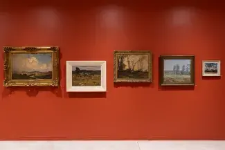 Five landscape paintings are hung against a vermillion wall. The frames are shifted up and down on the wall inorder to align the horizon lines of each different bucolic setting. 