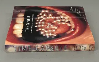 An almost sultry gaping mouth with cherry red lips and little silver coke balls scattered across the tongue takes up the cover of the book which rests on its back on a grey background. The title Time Capsule is written down the spine of the book and repeated on the cover just under the row of pearly white teeth, the words: A concise encyclopaedia by women artists, are written below. 