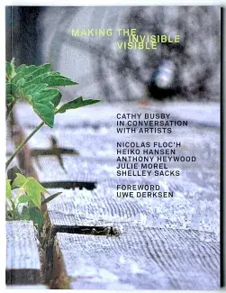 A closed focused image of few young green leaves peeking out from a void a wooden surface fills the front cover of the book. The title, Making the Invisible Visible is written in light green capital letters. Below in grey capitals reads Cathy Busby in conversation with artists Nicolas Floc’h, Heiko Hansen, Anthony Heywood, Julie Morel, Shelley Sacks. Foreword Uwe Derksen. 