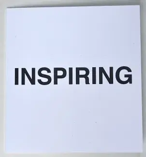  INSPIRING is written in bold black sans serif font across the center of a small square card stock folder. The block title asserts itself as a statement while withholding the context in it’s plainness. 