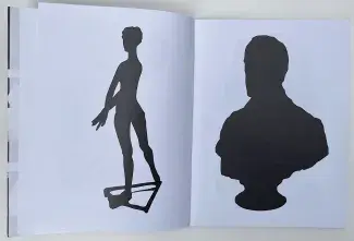 An open book; two xeroxed silhouettes in black ink, one on each white page, the left a long limbed feminine figure, the right a broad shouldered bust