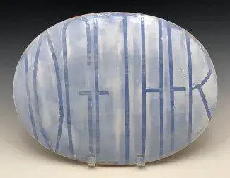 The backside of an ovular ceramic platter is painted in light blue and white. TOGETHER is written in thin tall lettering which swells to fit the convex shape.