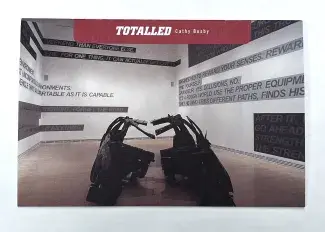  The image on the cover of the paper back publication is the frame of an SUV sliced down middle which is lying on a gallery floor. The walls of the gallery are lined with bold text against different coloured highlighted strips, the title TOTALLED Cathy Busby, is written on the top, white lettering on red highlight. 